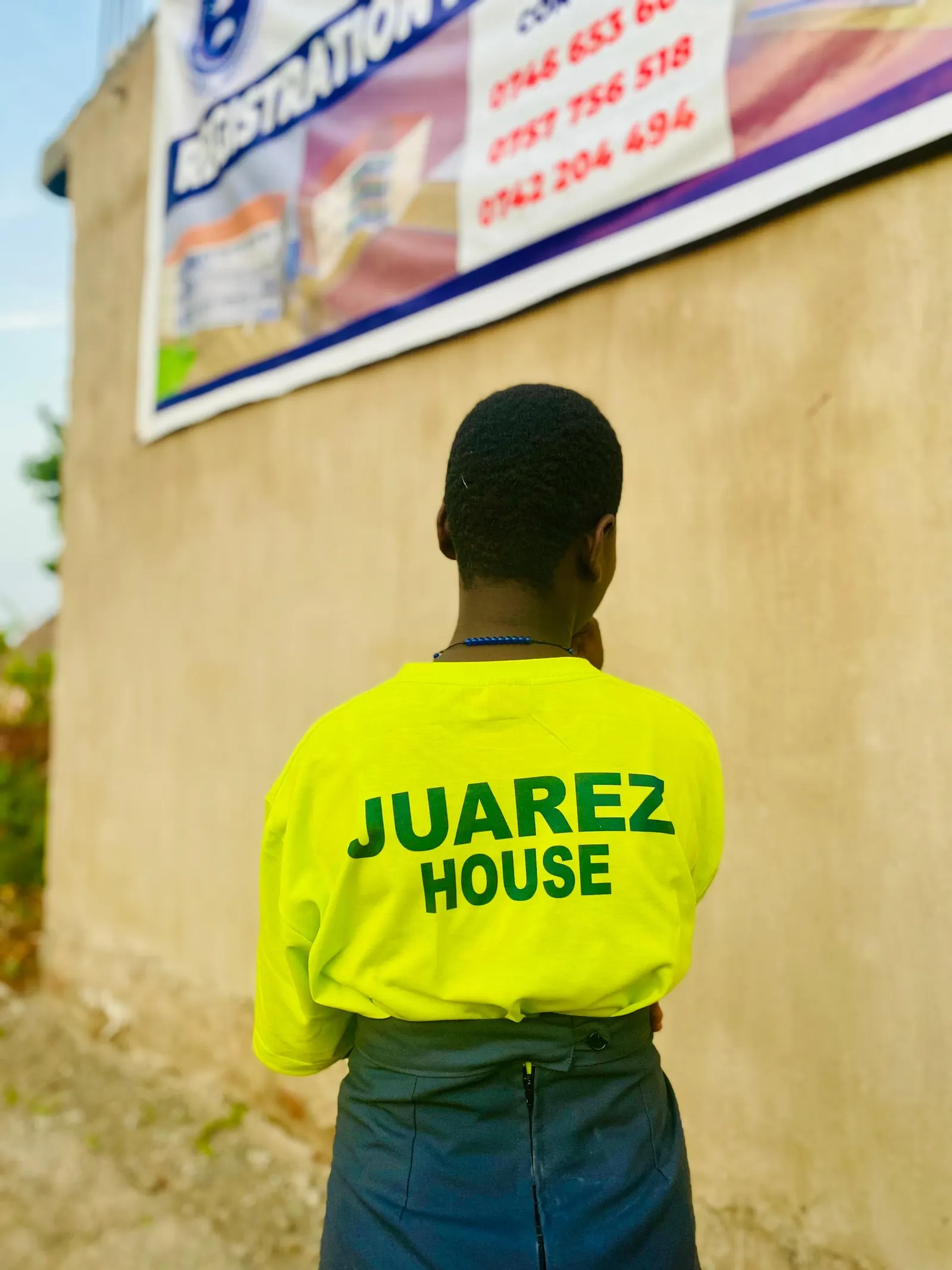 Student seen from behind wearing a yellow Juarez House t-shirt on the school grounds