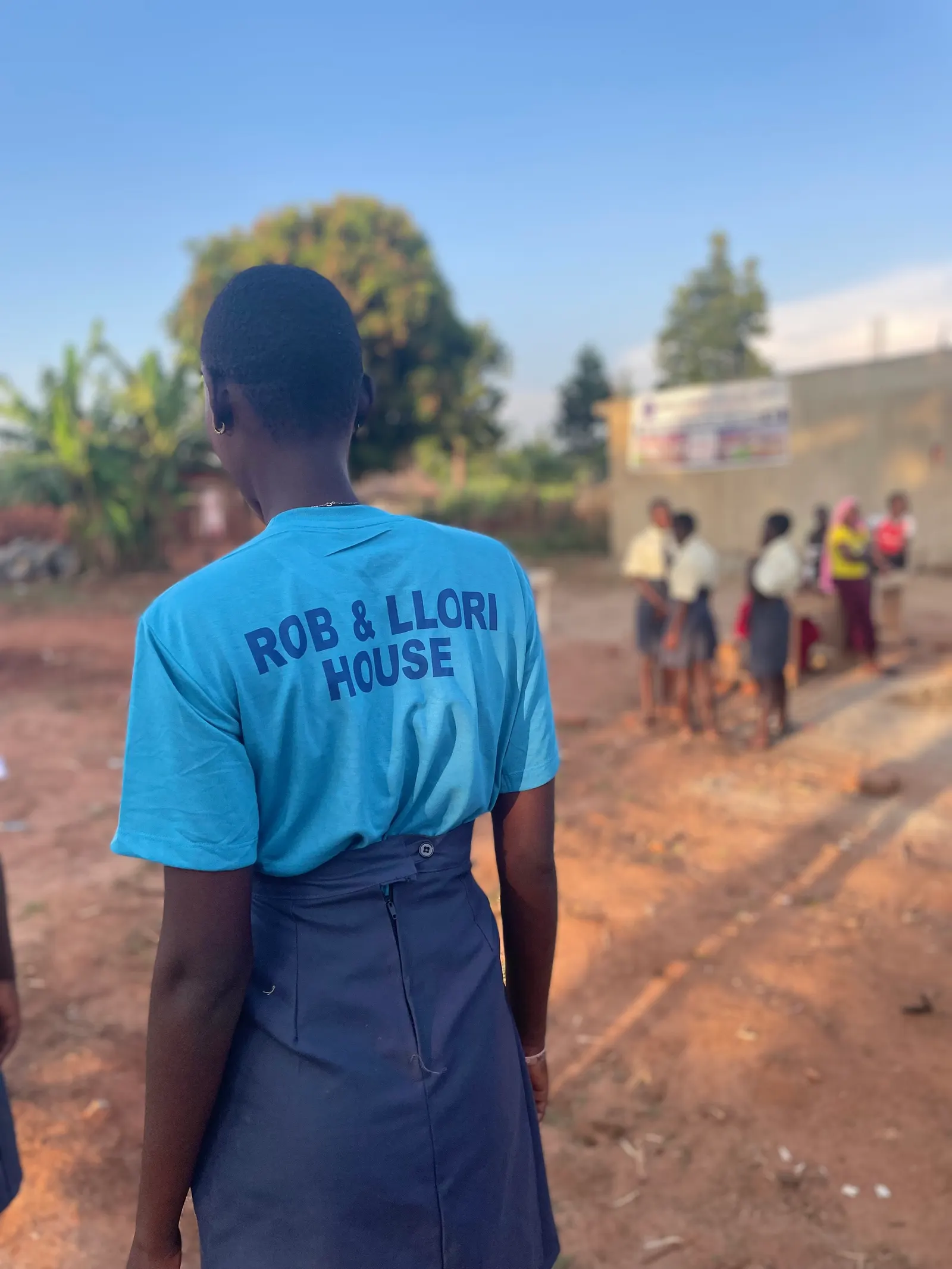 Student seen from behind wearing a blue Rob and Llori House t-shirt near the campus