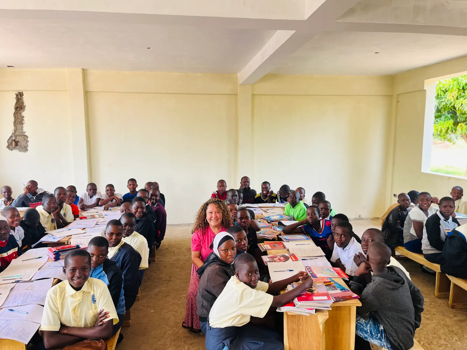 Students seated at desks in a classroom, a visitor standing among them