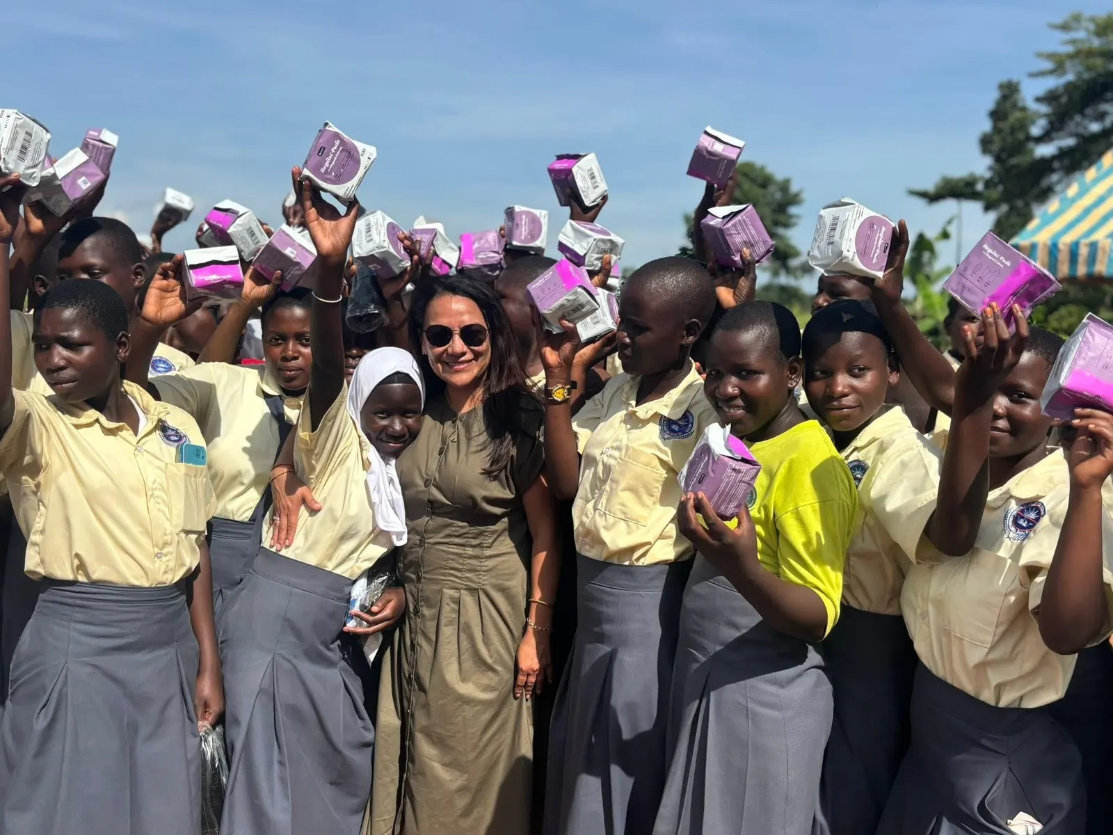 Students hold up donated sanitary pads beside a visitor
