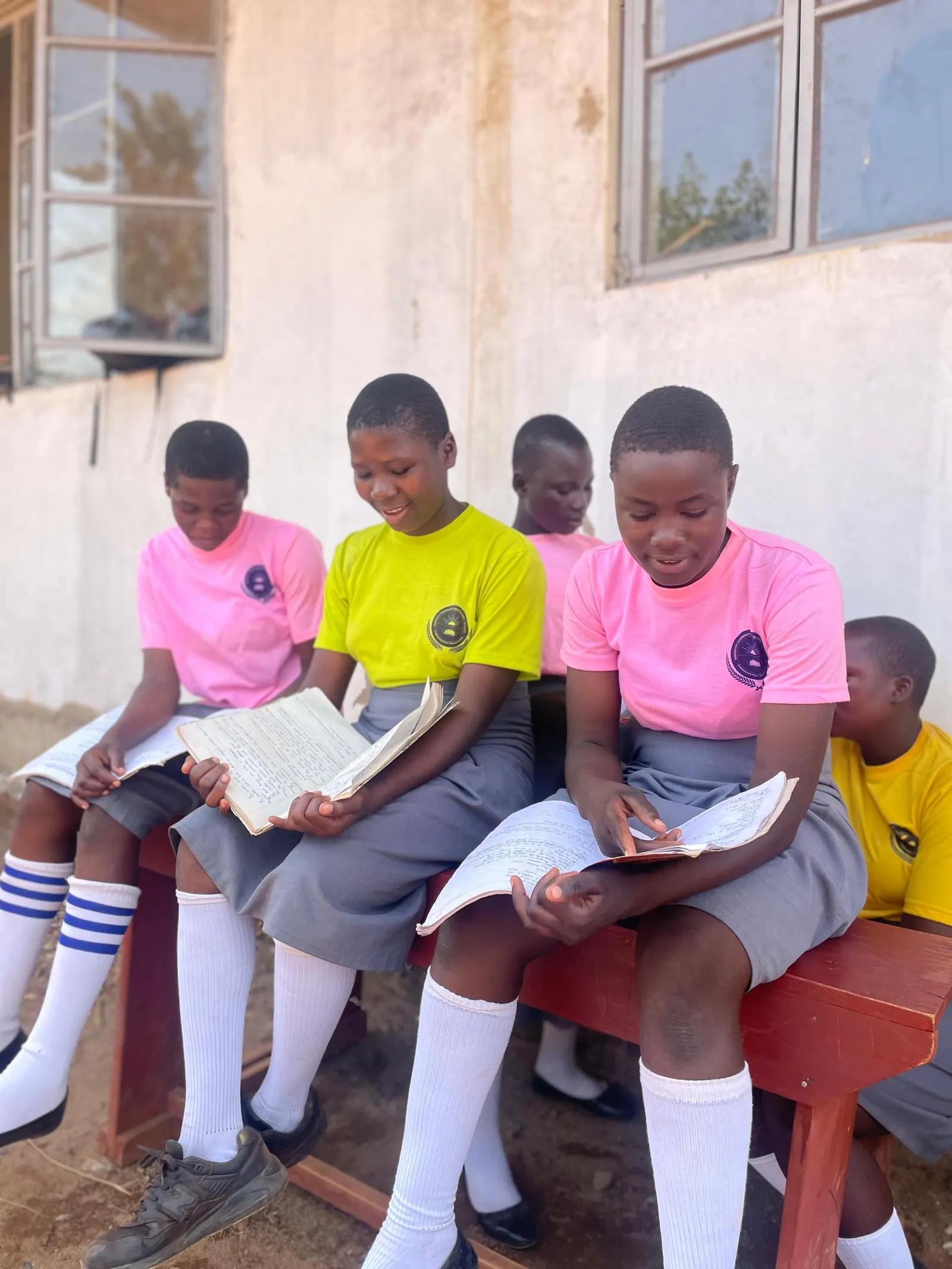 Four students reading textbooks together on a bench outside a classroom