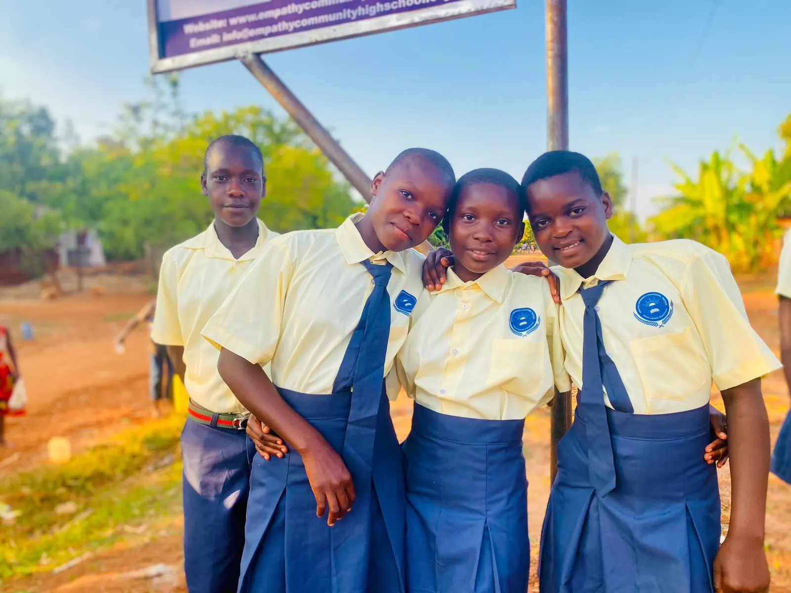 Four students stand arm in arm beneath the school signboard