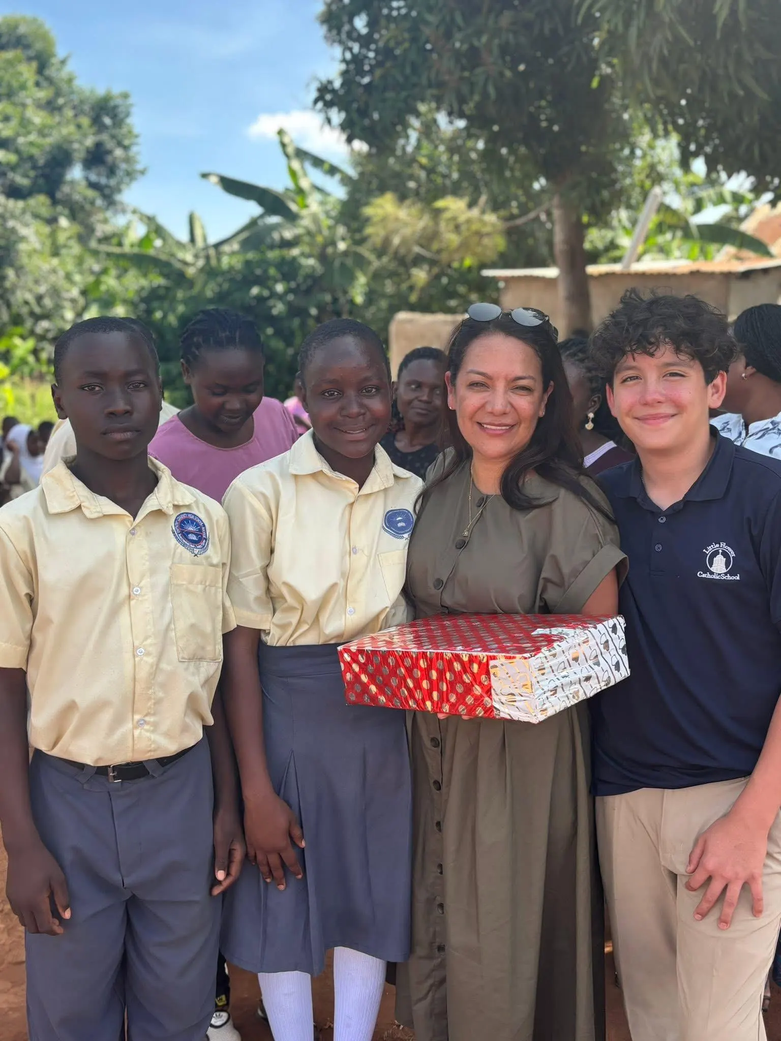 Visitors stand with students and hand over a gift box