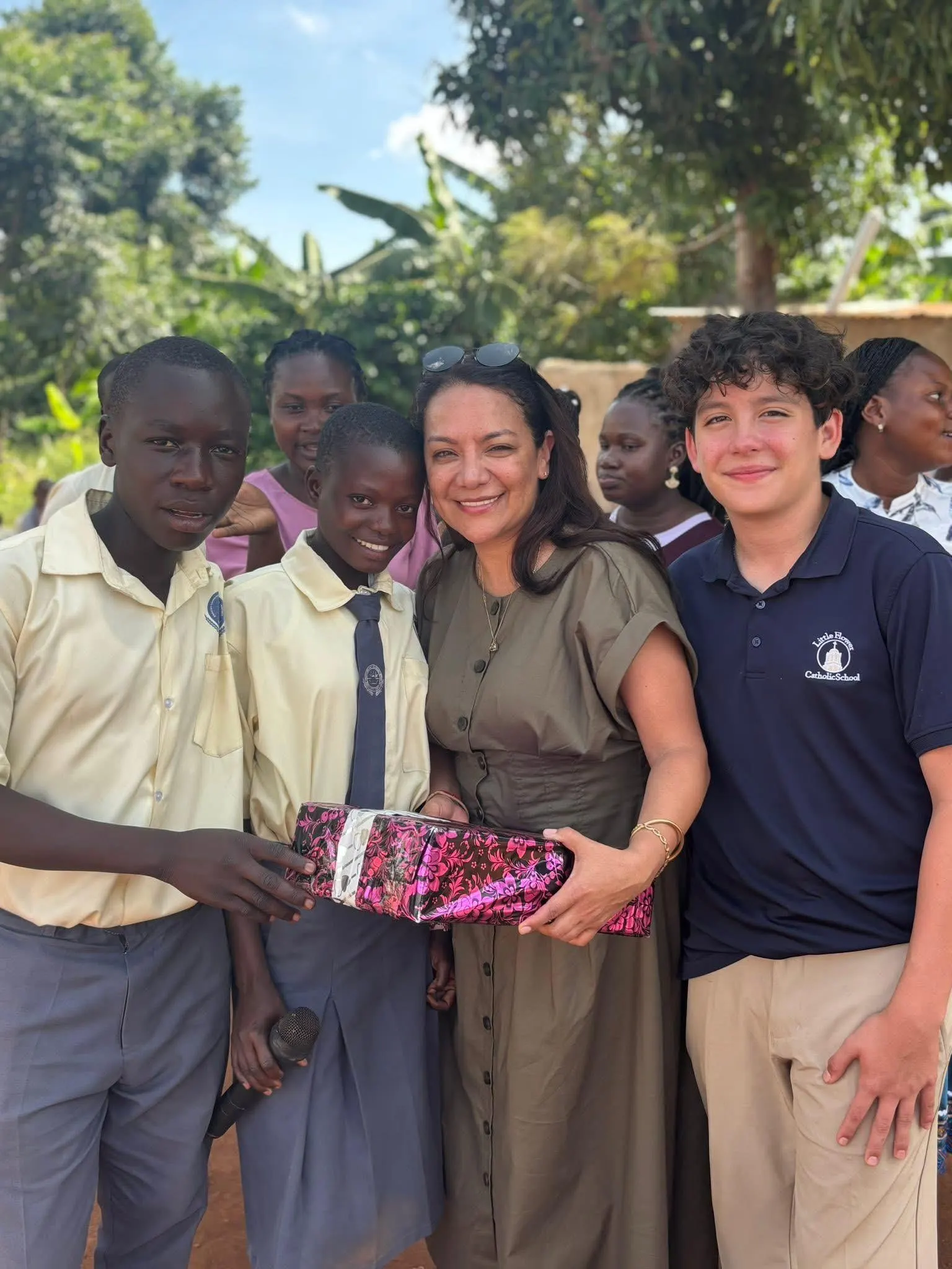 Visitors stand with students outside the classroom block holding a gift